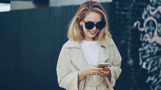 A young woman in sunglasses uses her smartphone.