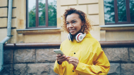 Young woman in yellow raincoat with headphones holding phone