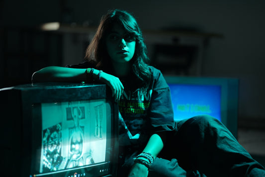 Teenager sits by vintage television in green light.