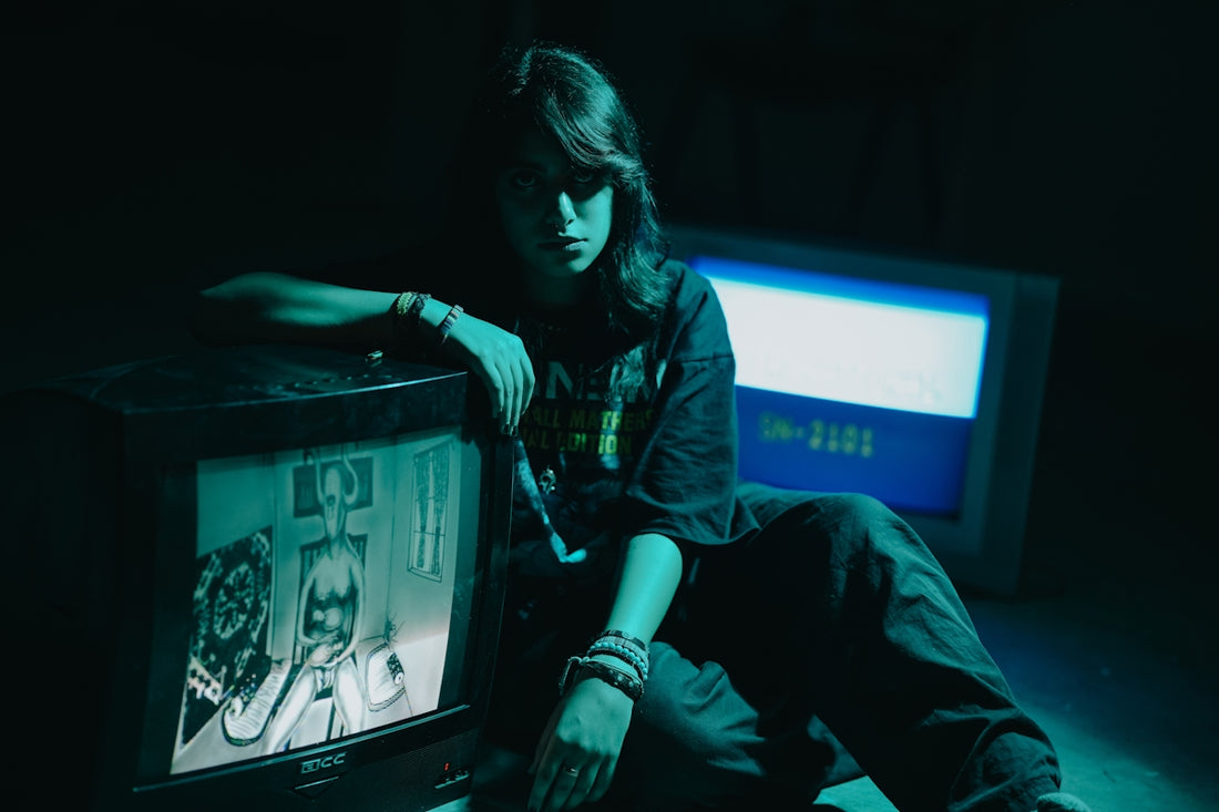 Teenager poses with vintage televisions in dark room.