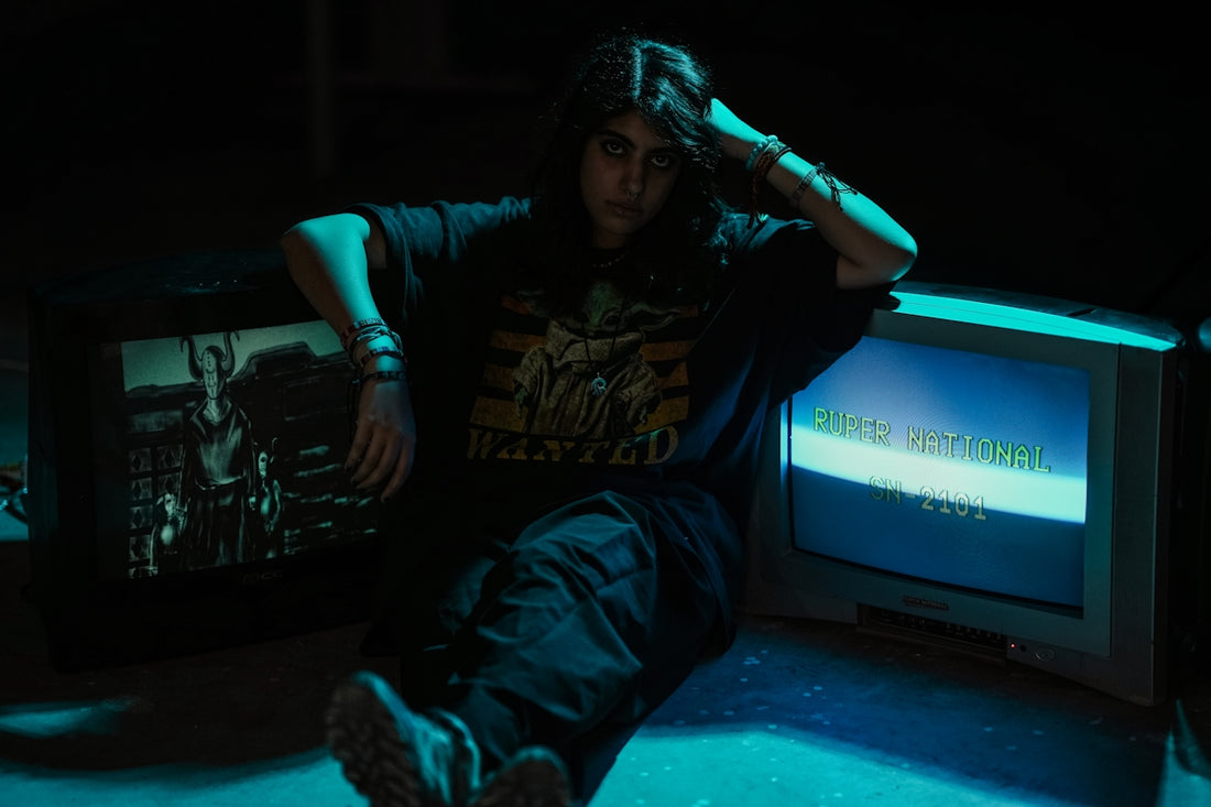 Young person with long hair sits between two old televisions.