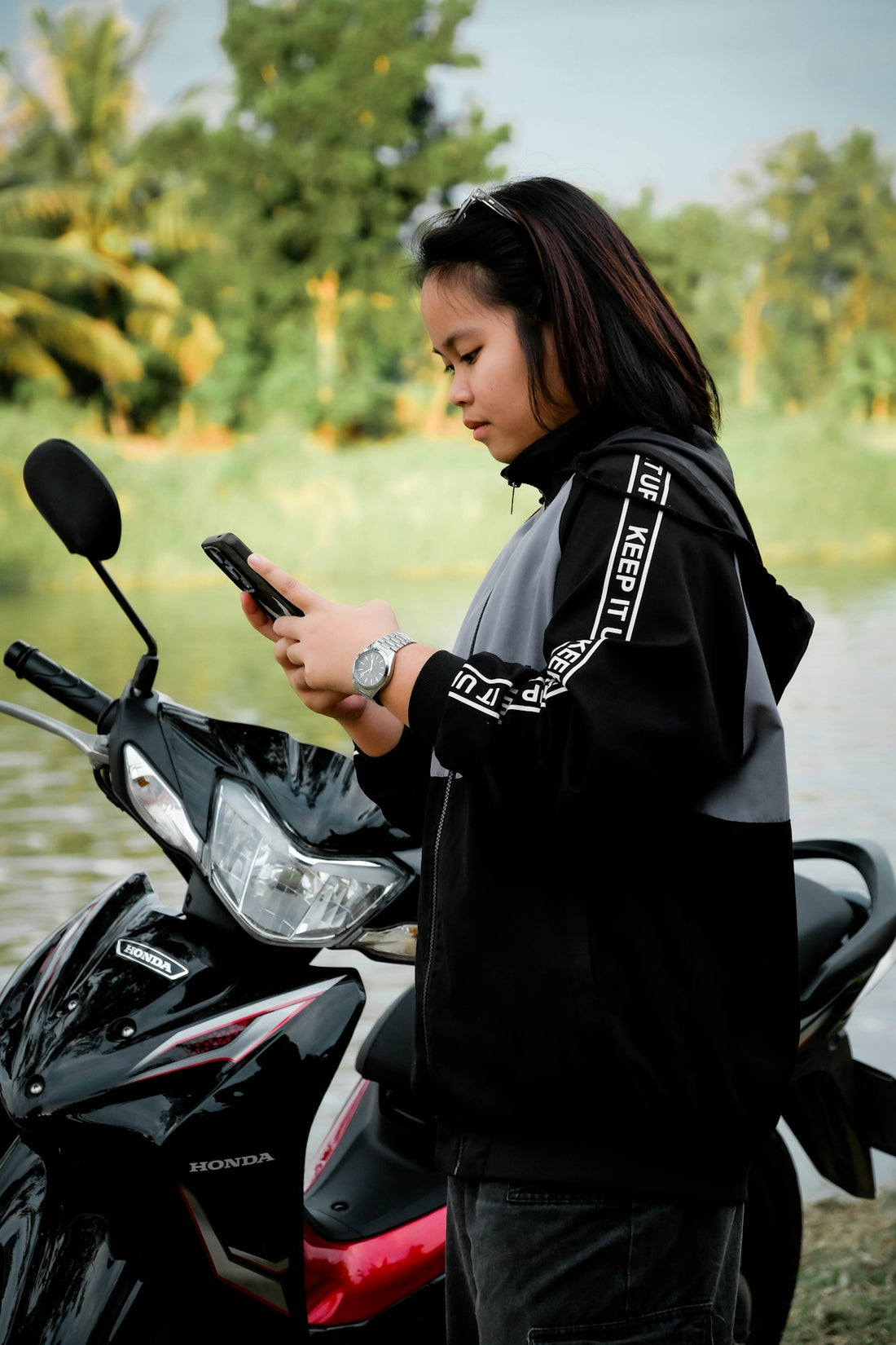 Young woman with phone by a motorcycle near water