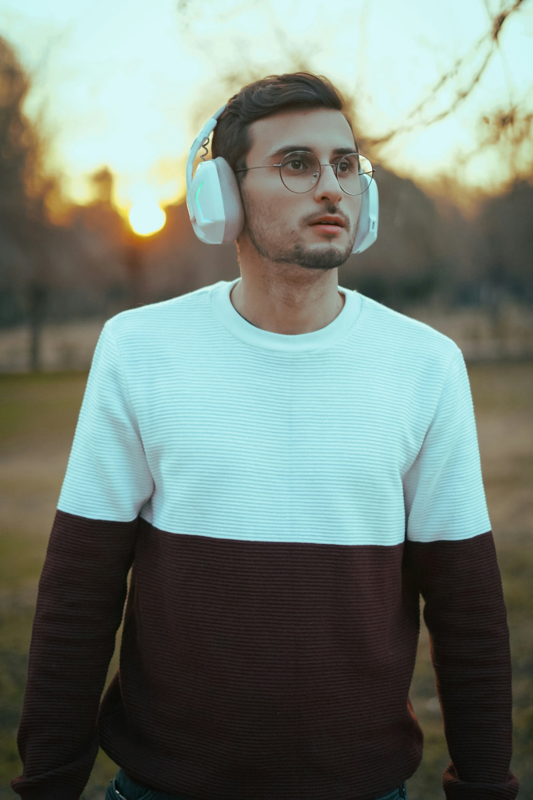 Man with headphones and glasses in park at sunset